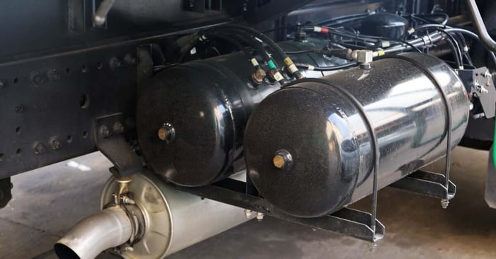 Black horizontal air receiver tanks mounted beneath a truck chassis with connected air lines and exhaust components.