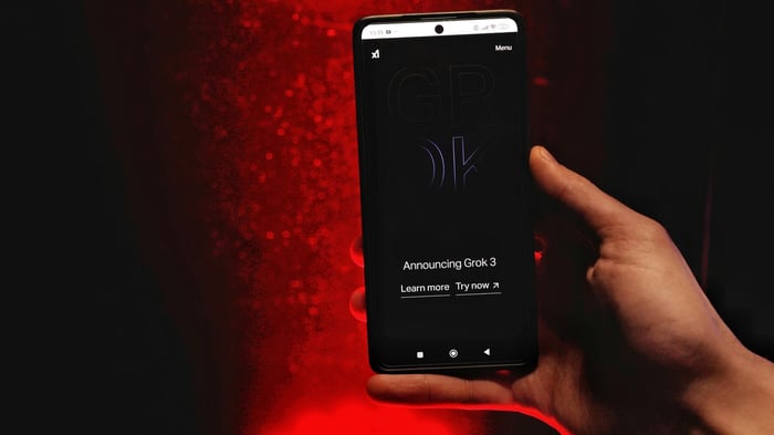 A hand holds a smartphone displaying Grok 3 announcement against a red background.