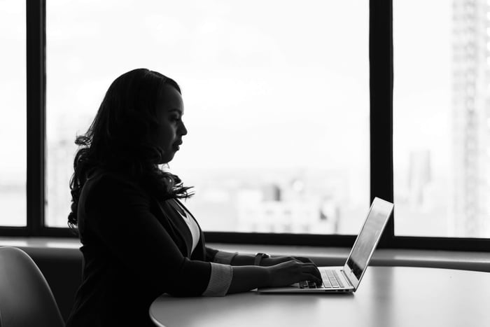 Black and white image of a woman working on her laptop in a modern office setting.