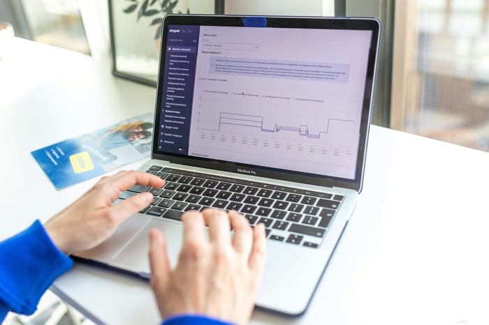 Hands typing on a laptop analyzing business data by a window, showcasing technology in action.