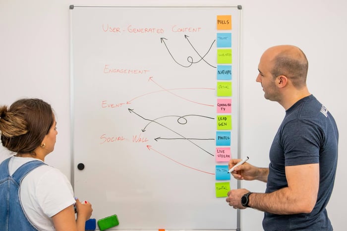 Two colleagues brainstorm ideas on a whiteboard during a creative strategy session.
