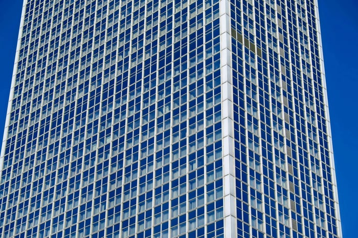 Tall glass skyscraper with a modern facade against a clear blue sky.