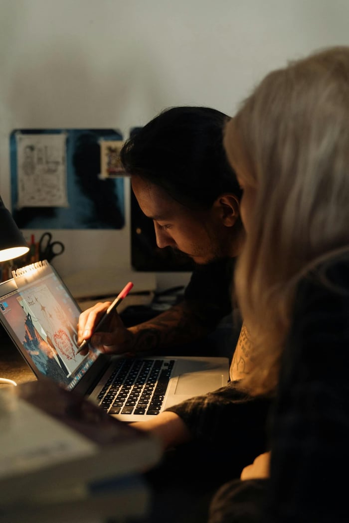 Two adults working on a creative project using a laptop at a desk indoors.