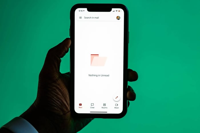 Close-up of a hand holding a smartphone displaying email app against a green background.