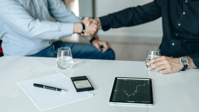 Business meeting with handshake and financial analysis displayed on a tablet.