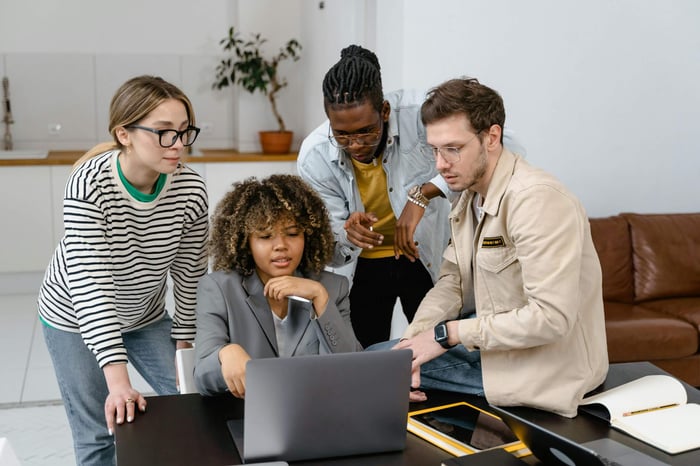 A group of diverse colleagues working together on a project around a laptop.