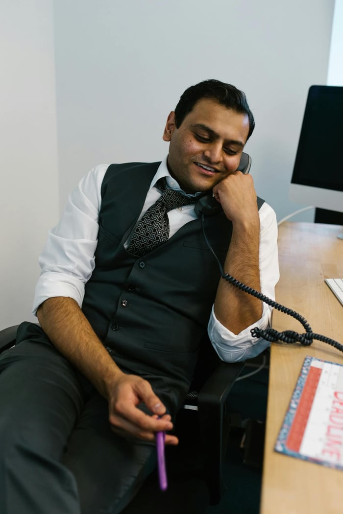 Smiling man in formal attire having a pleasant phone conversation in an office setting.