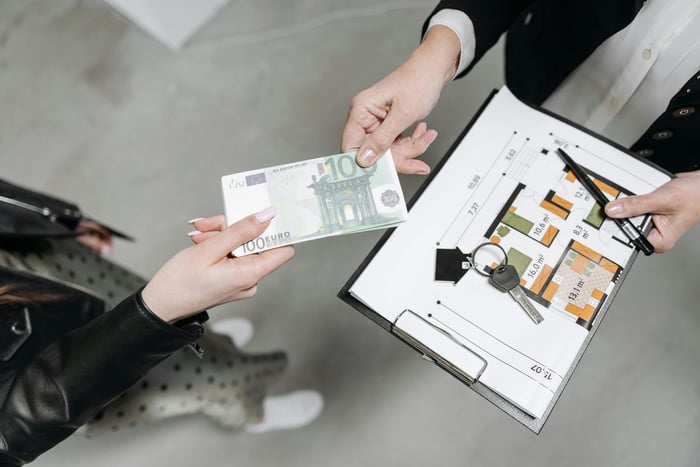 Close-up of a real estate transaction with euro bill, keys, and floor plan.