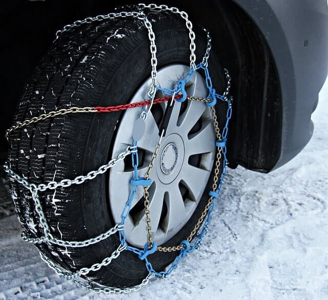 An image of a car's snow tire, complete with snow chains to help the car stay on the road.
