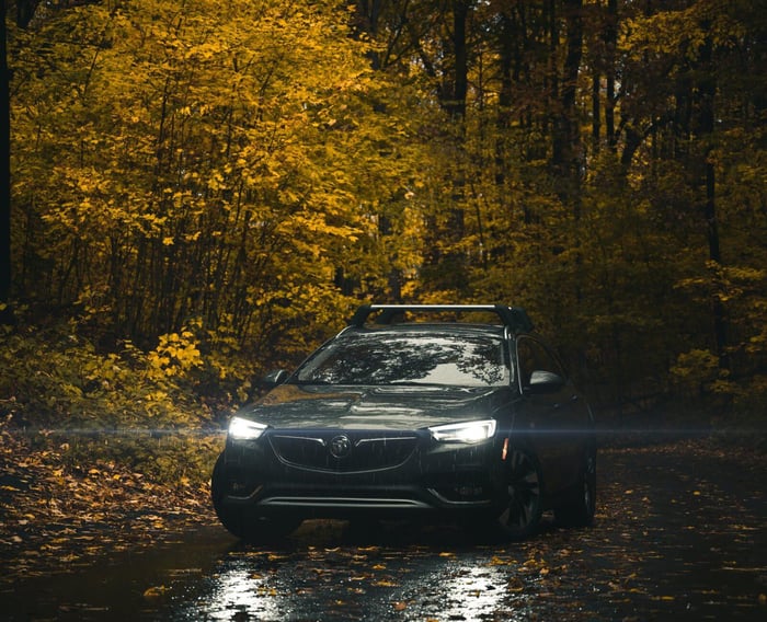 Black used car driving through rainy woods.