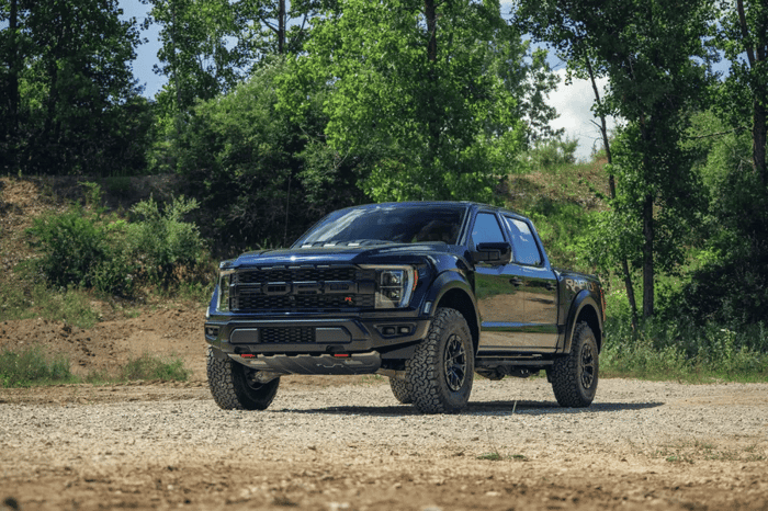 Black Ford F150 diesel vehicle parked in front of trees on a gravel road.