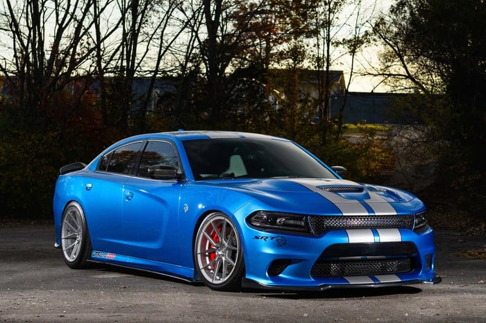 Blue Dodge Charger SRT parked on pavement in front of trees, with a building in the background.