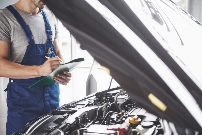 Mechanic performing an insepection on truck with open hood.
