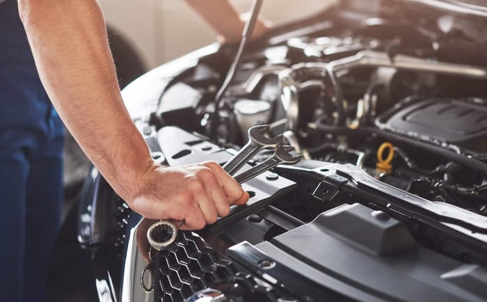 Open hood with mechanic standing in front with tools in hand.