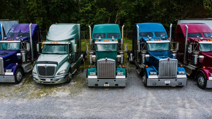 Line up of multi-colored trucks parked along a patch of grass.