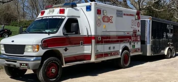 An ambulance turned work truck carrying a trailer.