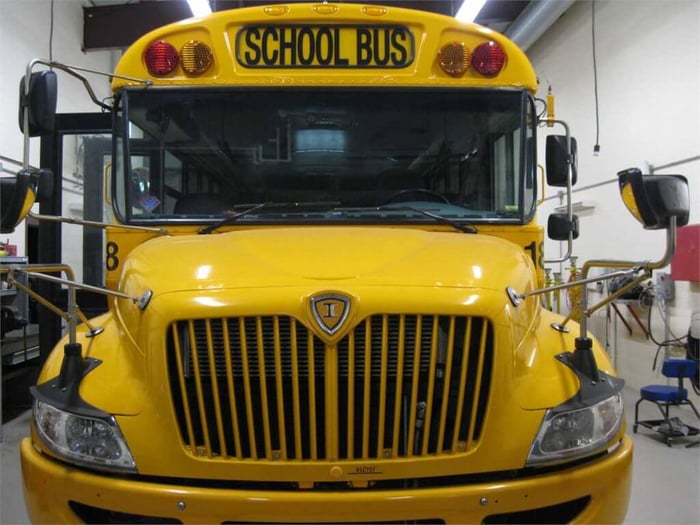 A front view of a yellow school bus, sitting in a garage. The school bus is a little older, with a very defined front hood.
