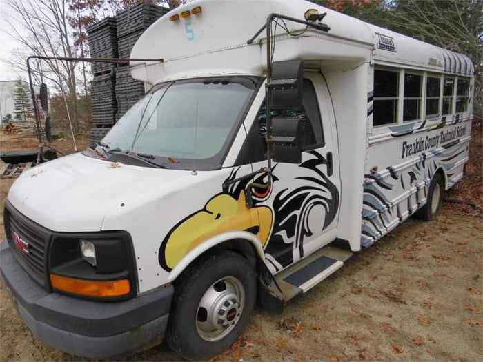A white Type A bus at a 3/4 view angle. The bus is a decommissioned bus from Franklin County Technical School; it's white, and painted with eagles and feather-like patterns.