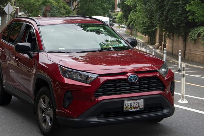 A red Toyota Highlander driving down a tree-lined street.