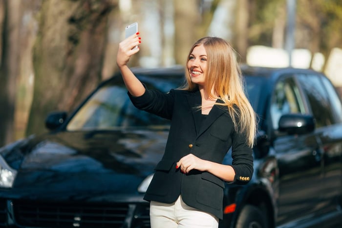 Influencer taking a selfie beside a new car.