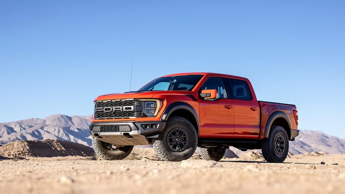 Bright orange Ford F 150 parked in the desert with standard specs, regular cab bed measuring 96 inches long, and space for stuff in the back.