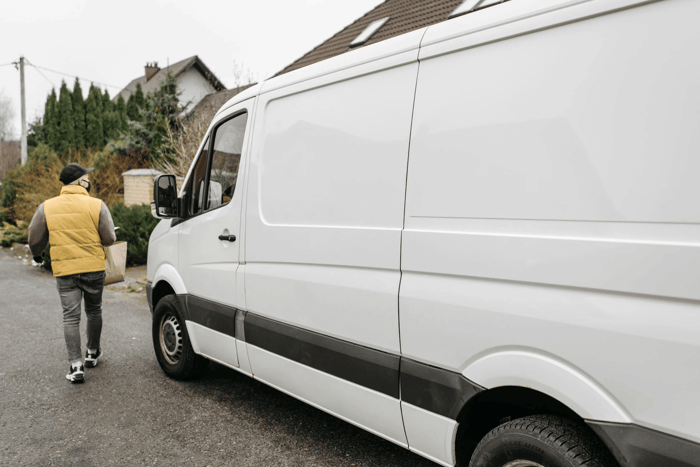 Delivery man carrying box beside parked van.