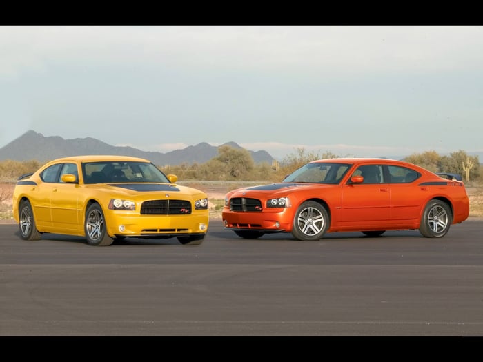 Yellow and orange Dodge Chargers in a parking lot at sunset.