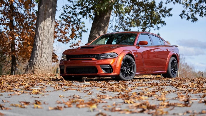Orange Dodge Charger SRT, parked by trees with leaves on the ground, providing both durability and luxury.