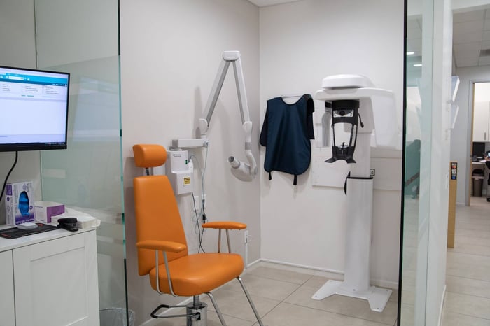 Dental imaging room with orange chair, wall-mounted X-ray arm, and 3D dental scanner used for patient diagnostics.