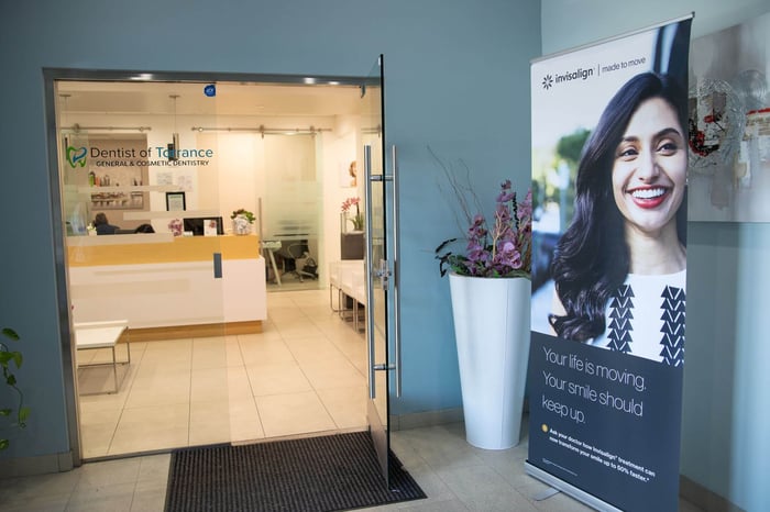 Dental office entrance with glass doors, front desk visible inside, and Invisalign promotional banner near the doorway.