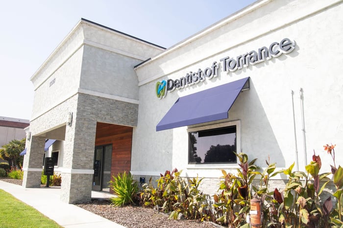 Exterior of Dentist of Torrance building with modern white facade, blue awning, signage, and landscaped walkway.