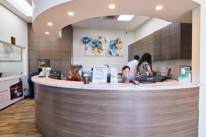 Modern dental office reception desk with friendly staff assisting patients in a bright waiting area.