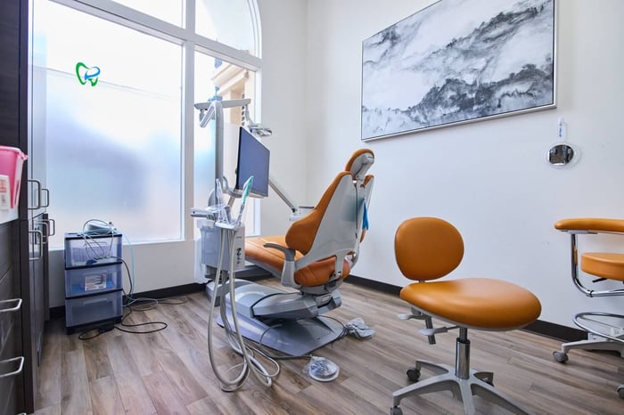 Bright dental treatment room with modern orange dental chair, equipment, and natural light.