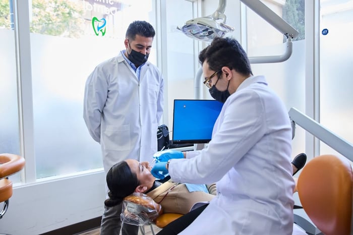 Dentists wearing masks performing a dental procedure on a patient in a modern treatment room.