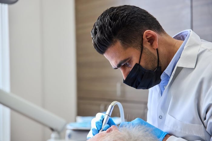 Dentist wearing a mask and gloves carefully performing a dental procedure in a treatment room.