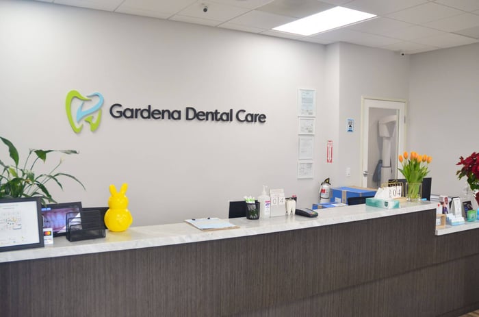 Front desk and reception area at Gardena Dental Care with logo on wall, clean countertop, and welcoming office decor.
