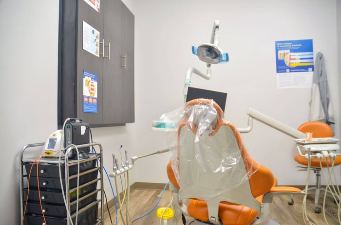 Dental treatment room with orange patient chair, overhead exam light, instruments, and cabinets at Gardena Dental Care.
