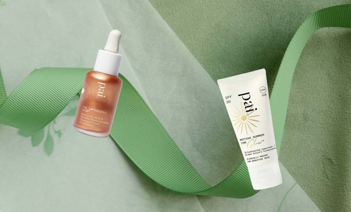 The Impossible Glow bronzing drops and British Summer Time SPF 30 sunscreen arranged on green ribbon against sage backdrop