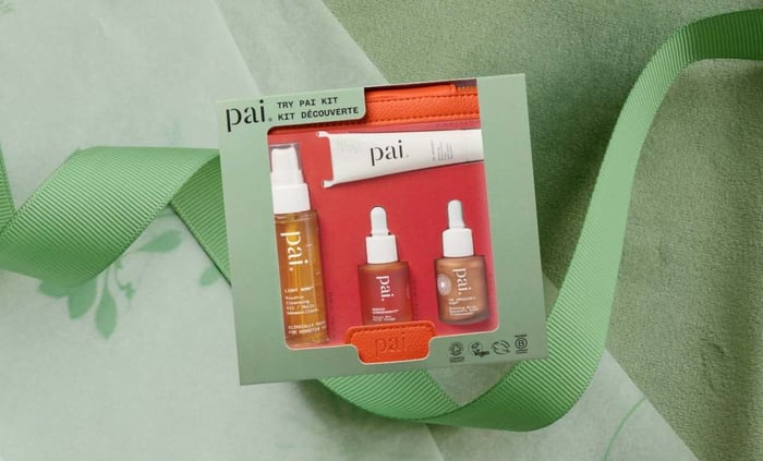 Pai Try Pai Kit skincare gift set with travel-size cleanser and serums, surrounded by green ribbon on textured background