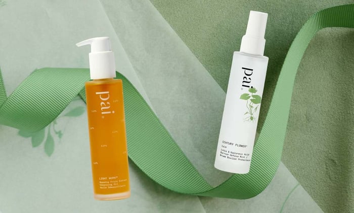 Pai Skincare Light Work Rosehip Cleansing Oil and Century Flower Toner arranged with green ribbon on sage background