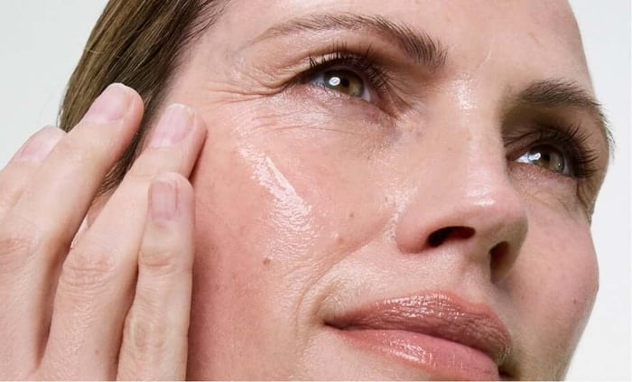 Close-up of woman applying moisturizer to face showing healthy glowing skin texture
