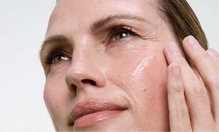 Woman applying anti-aging serum to her face, showing smooth hydrated skin texture