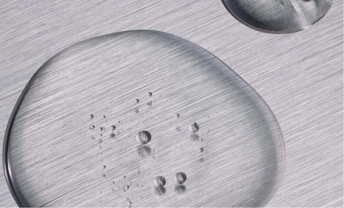 Clear serum droplets beading on brushed metal surface showing lightweight texture