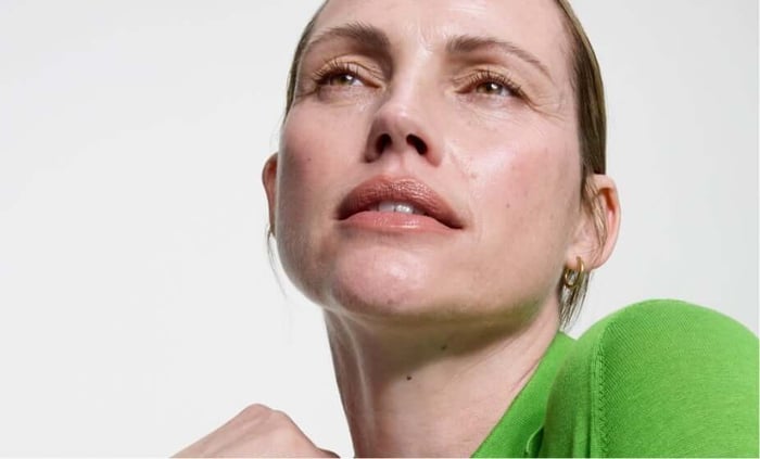 Woman with radiant, healthy-looking skin wearing bright green top against neutral background