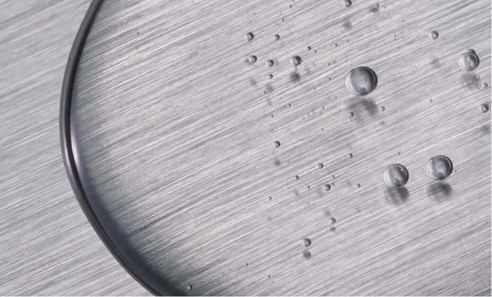 Clear water droplets on brushed metal surface demonstrating hydration and cellular protection