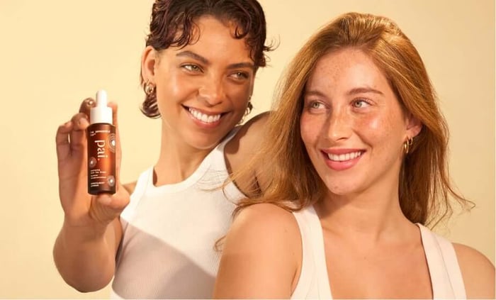 Two smiling women holding Pai natural self tan drops for sensitive skin against warm beige background