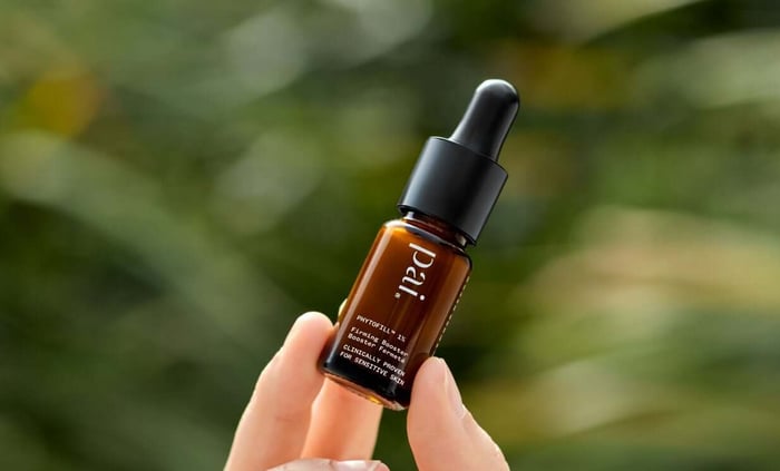 Pai Phytofill 1% Firming Booster with amber glass bottle and dropper held in hand against green foliage