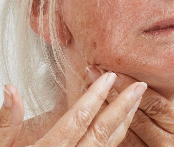 Close-up of mature woman with blonde hair applying natural skincare to face with gentle touch