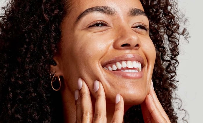 Smiling woman with curly hair touching her glowing, healthy skin after using natural skincare products