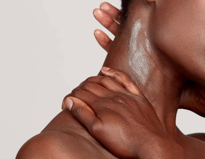 Hands applying white cream moisturiser to dark skin in gentle circular motions for body care routine